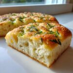 Close-up of a thick, airy slice of homemade Rosemary focaccia bread topped with sea salt.