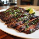 Close-up of juicy, sliced Carne Asada steak, garnished with fresh cilantro and lime wedges.