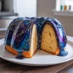 A sliced bundt Galaxy cake featuring a vibrant, shimmering blue and purple mirror glaze resembling a starry night sky.