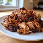 Close-up of a mound of juicy, shredded Smoked oven-braised pulled pork on a white plate.