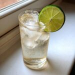 A tall glass filled with ice and bubbly liquid, garnished with a fresh lime wheel, representing Smoked Ranch Water.