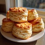 A stack of freshly baked, tall Southern buttermilk biscuits with golden tops and visible layers.