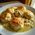 Close-up of fluffy, golden-topped dumplings served in creamy gravy with shredded chicken for Southern chicken and dumplings.