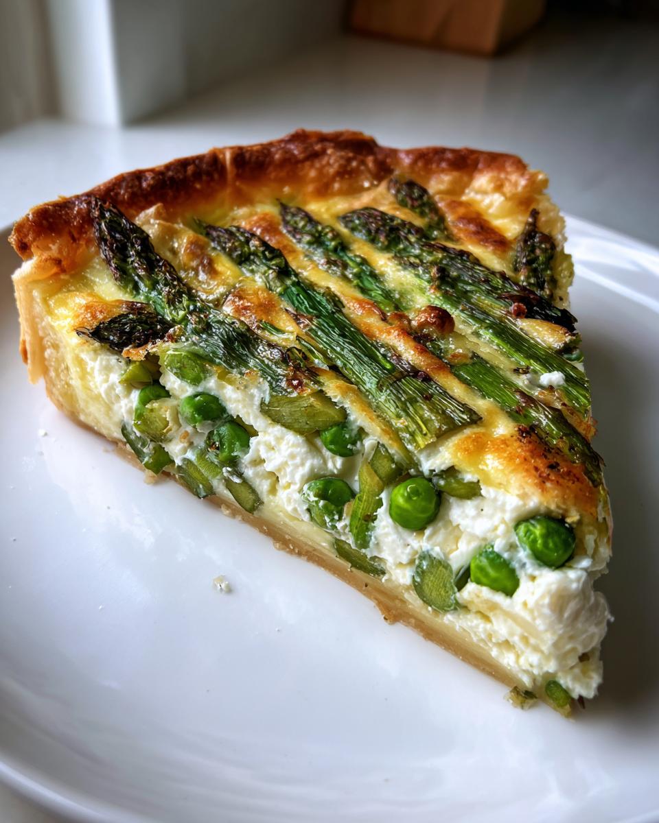 A close-up slice of a Spring vegetable tart featuring bright green asparagus spears and peas set in a creamy white filling.