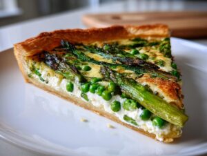 A close-up slice of a golden-crusted Spring vegetable tart filled with ricotta, bright green peas, and roasted asparagus spears.