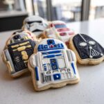A close-up of several decorated Star Wars sugar cookies, featuring R2-D2, Darth Vader, and Stormtrooper designs.