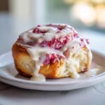 A single, fluffy Strawberry crunch cinnamon rolls topped with bright pink filling and dripping with thick white icing.