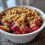 Close-up of a warm serving of Strawberry Rhubarb Crumble with a golden, crunchy topping over bright red fruit filling.