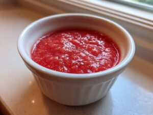 A close-up view of vibrant, textured strawberry rhubarb sauce served in a small white ramekin.
