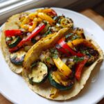Two soft corn tortillas filled with grilled summer squash, red and yellow peppers, and onions for amazing summer squash sheet pan tacos.