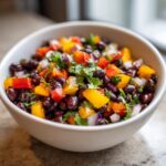 Close-up of a white bowl filled with colorful Cowboy Caviar, featuring black beans, yellow and red peppers, and red onion.