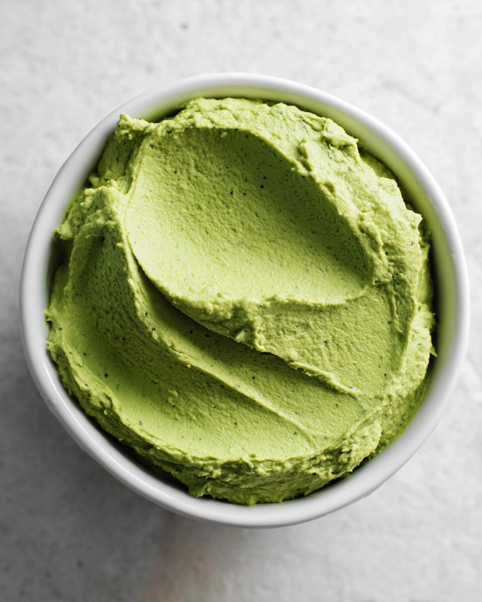 Overhead close-up of thick, bright green Greek goddess dip swirled in a white serving bowl.