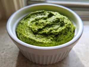 Close-up of a vibrant green, thick Greek goddess dip served in a small, white, fluted ramekin.