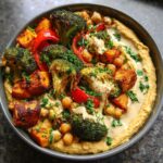 A vibrant Hummus bowl topped with roasted broccoli, sweet potatoes, red peppers, chickpeas, and a creamy tahini drizzle.