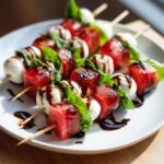 Close-up of several Watermelon Caprese Skewers featuring cubes of watermelon, mozzarella balls, and basil, drizzled with balsamic glaze.