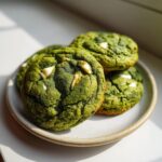 A stack of vibrant green White Chocolate Chip Matcha Cookies with visible white chocolate chunks on a light ceramic plate.
